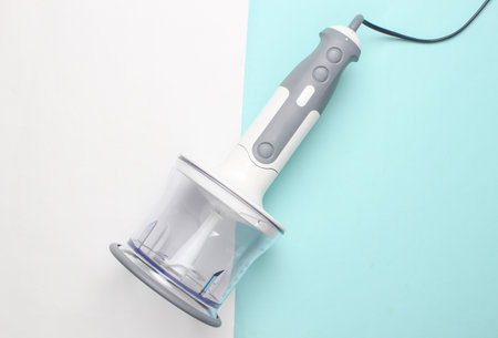 Electric hand blender attached to chopping bowl on blue white background. Top view