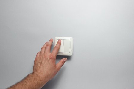 Hand presses a light switch on gray wall backgroundの写真素材