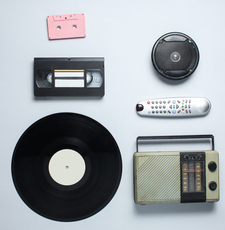 Radio receiver, vinyl record, audio cassette, video cassette, tv remote on a gray background. Retro...