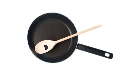Wooden spatula for cooking with cut out heart in nonstick frying pan isolated on white background. Top viewの写真素材