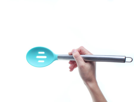 Hand holds silicone cooking spoon with metal handle. Isolated on a white background. Top view.の写真素材