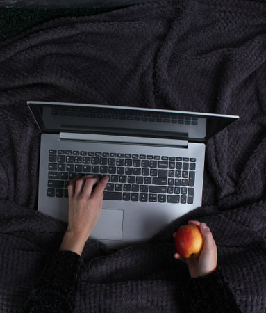 Female legs wrapped in blanket sit and use a laptop. Winter morning, working space. Cozy and warm workplace, online work. Top viewの写真素材