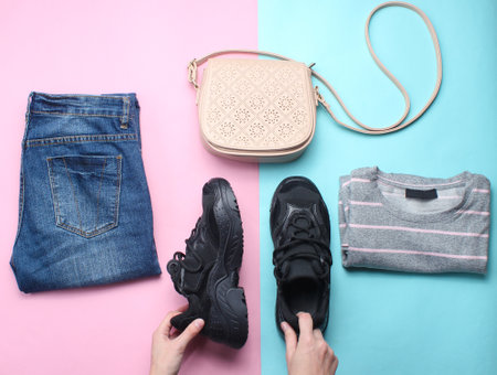 Women's accessories, clothing shoes on a pastel background. Jeans, sweater, bag. Women's hands hold sneakers. Creative flat lay. Top view. minimalismの写真素材