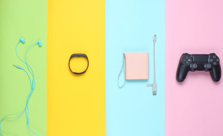Power bank and usb cable, gamepad, smart bracelet, earphones on colored pastel background. Modern gadgets. Top view, minimalism.の写真素材