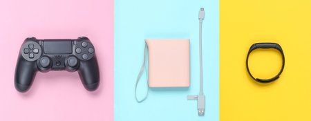 Power bank and usb cable, gamepad, smart bracelet on colored pastel background. Modern gadgets. Top...