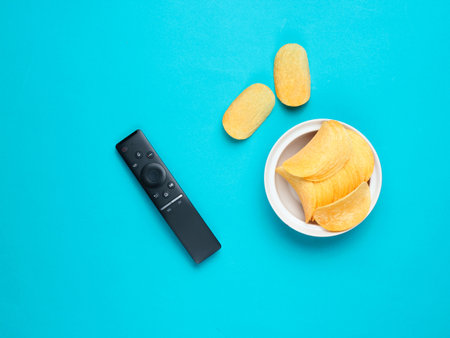 Tv remote, potato chips in a plate on bue background. Watching TV, top viewの写真素材