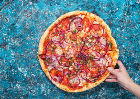 The hand takes a piece of homemade pizza on a blue concrete background. Top viewの写真素材