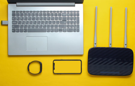 Laptop, router, smartphone, smart tracker, on yellow background. Online work, gadgets for modern peopleの写真素材