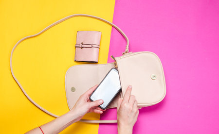 Women's hand takes smartphone from leather bag on colored paper background. Top view, flat lay, minimalismの写真素材