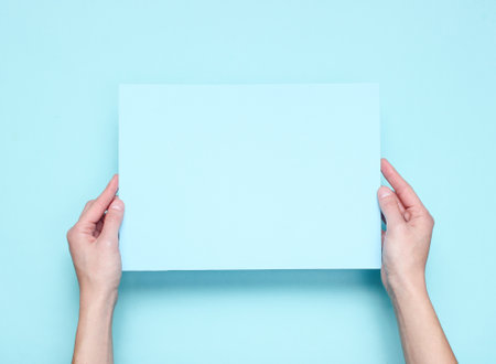 Female hands holding blue paper sheet on blue background. Top view. Mockup, copy space, minimalismの写真素材