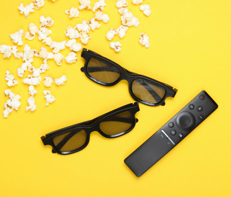 Two pairs 3D glasses, TV remote, popcorn on a yellow background. Top view, flat layの写真素材