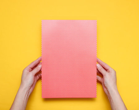 Female hands holding paper sheet with polka dot on yellow background. Top view. Mockup, copy space,...