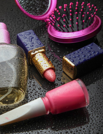 Red lipstick, perfume bottle, nail polish, mirror comb with water drops on a dark black background. Beauty and fashion.の写真素材