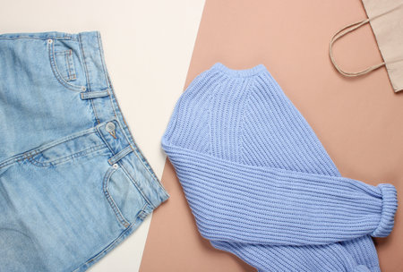 Flat lay style knitted sweater, trendy blue jeans, paper bag on pastel background, top view, minimalism, copy spaceの写真素材