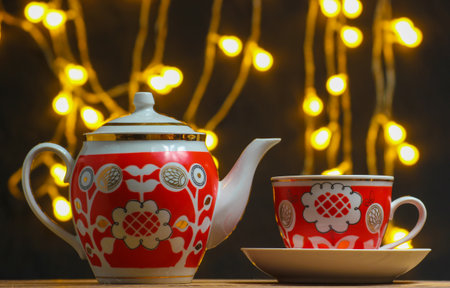 Retro ceramic cup and teapot on dark blurred background with light bulbs.の写真素材