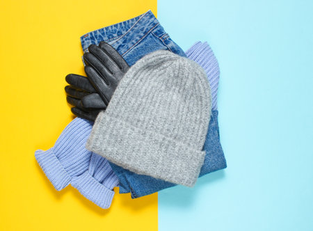 Women's clothing and accessories. Winter woolen hat, sweater, leather gloves, jeans on colored paper background, minimalism, top view, flat lay styleの写真素材