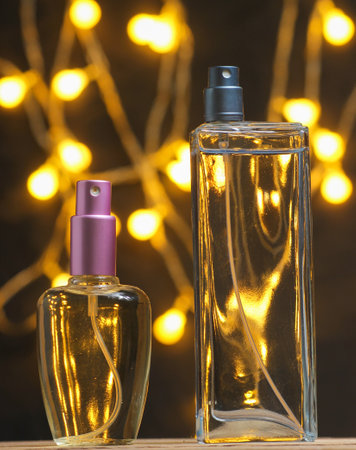 Two perfume transparent glass bottles on dark blurred background with garlands.の写真素材