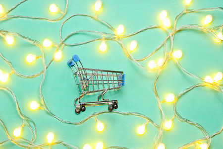Mini shopping trolley with bright garlands on blue background. Christmas sale. Top view, minimalism
Â の写真素材