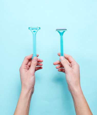 Women's hands hold two shaving razor for epilation on a blue background. Top view, minimalism, flat lay styleの写真素材