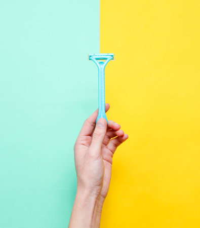 Female hand holding razors for epilation on a blue yellow background. Top view, minimalism, flat lay styleの写真素材
