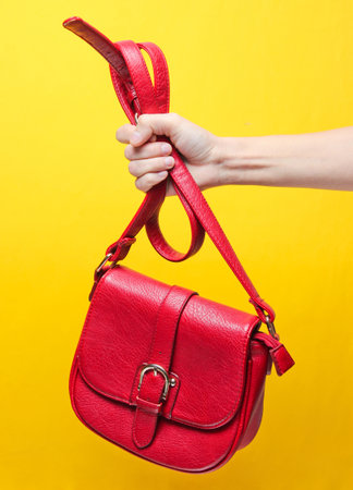 Female hand holding red leather bag by the strap on a yellow background. Minimalismの写真素材