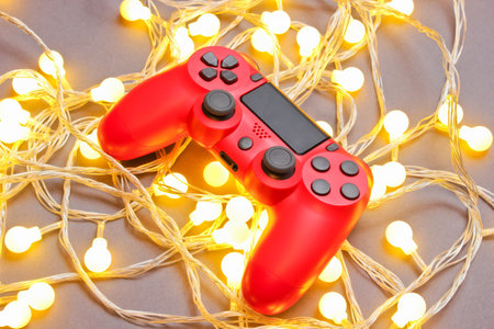 Red gamepad among glowing bright garlands on gray background. Minimalism
