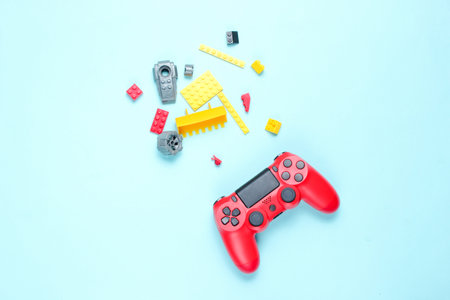 Children's 80s entertainment on blue background. Red gamepad, children's constructor bricks, top view, minimalismの写真素材