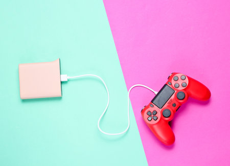 Modern red plastic gamepad is charging from  power bank on colored neon background. Top view. Minimalismの写真素材
