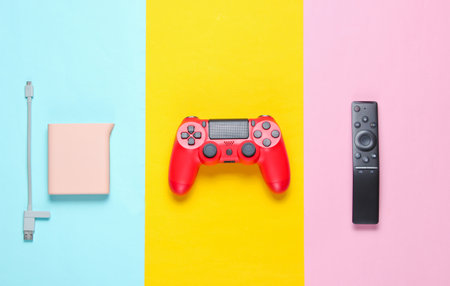 Power bank, red gamepad, tv remote on a colored paper background. Top view. Modern gadgets and accessories for recreation.の写真素材