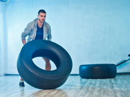 Young sports man raises a large weight wheel. training process. Functional trainingの写真素材