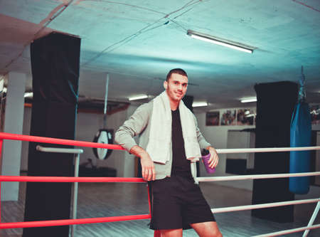 Rest boxer in the ring. Young boxer man with towel around his neck smiles while resting near the sides of the ring.の写真素材