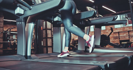 Female muscular feet in sneakers and leggins running on the treadmil at gym. Cardio training