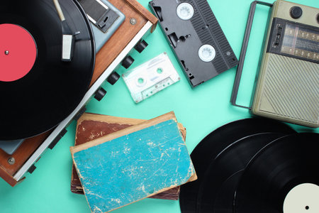 Retro attributes, 80s media. Vinyl player, video cassettes, audio cassettes, records, radio, old books on blue background. Top viewの写真素材