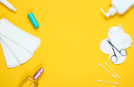 Copy space women's beauty and hygiene products on yellow pastel background. Perfume bottle, hygienic lipstick, pads, bottle cream,nail scissors. Flat lay styleの写真素材