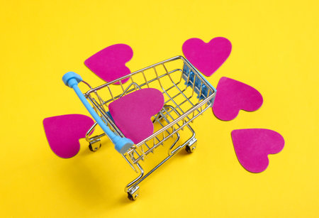 Mini shopping trolley, decorative hearts on yellow background. Conceptual photoの写真素材