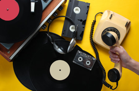 Retro attributes from the 80s on yellow background. Female hand holds the handset of vintage rotary...