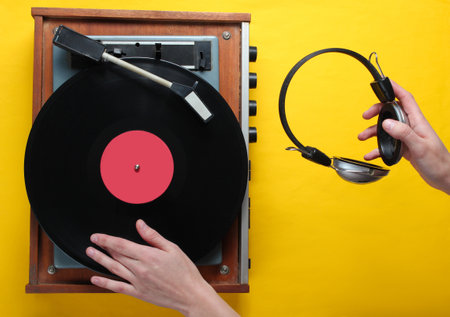 Retro style, DJ plays vinyl record player and holds headphones in hand, minimalism, top view on yellow backgroundの写真素材