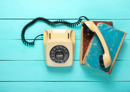 Retro rotary telephone on a blue wooden table. Handset on stack of old phone booksの写真素材