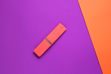 TV remote control in a red silicone case on a purple orange paper background. Minimalism, top view