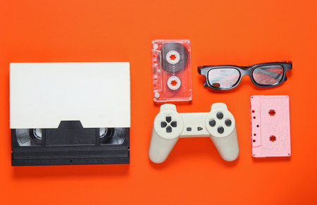 Pop culture attributes. audio cassette, retro gamepad, video tape, 3d glasses on a orange...