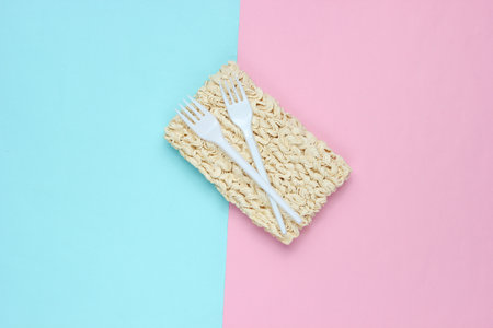 Raw instant noodles and plastic forks on a pastel background, minimalism, top view