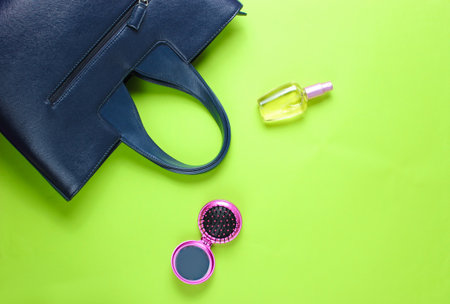 Women's accessories. Leather bag, perfume bottle, comb-mirror on green paper background. Top view. Copy spaceの写真素材