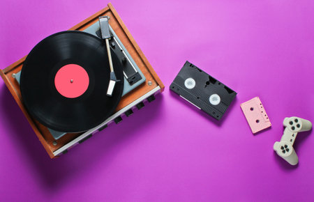 Retro items on a pink background. Vinyl player, video, audio cassette, gamepad. Pop culture, 80s. Top viewの写真素材