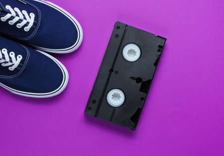 Retro style stuff 80s. Videotape, jeans, sneakers on purple background. Top viewの写真素材