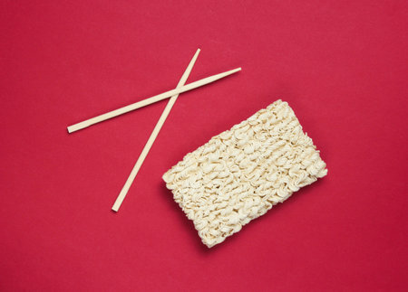 Raw instant noodles and chinese chopsticks on red background, minimalism. Top viewの写真素材