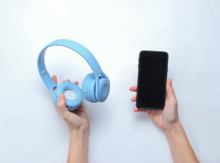 Female hands holding modern smartphone and headphones on gray background. Sync gadgets, interaction. Top viewの写真素材