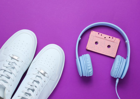 Retro style. 80s. Pop culture. Minimalismalism. Headphones with audio cassette, white sneakers on purple background. Top viewの写真素材