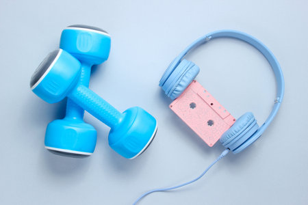 Sport equipment. Retro style. Blue plastic dumbbells, headphones with audio cassette on a gray background. Top view.の写真素材