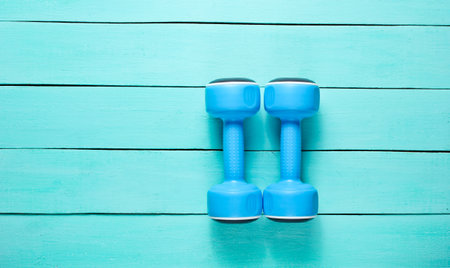Two plastic blue dumbbells on blue wooden background. Top view.の写真素材