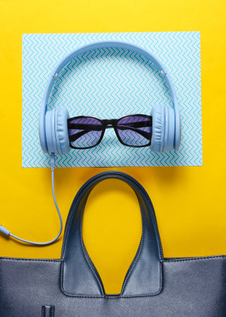 Fashionable youth accessories. Headphones, sunglasses, women's leather bag on a yellow-blue creative background. Top view. Minimalismの写真素材